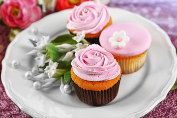 Tasty cupcakes on plate, on color wooden background