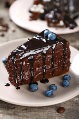 Chocolate cake with chocolate cream and fresh blueberries on plate, on wooden background