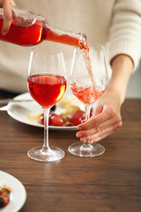 Young woman pouring pink wine into glass on the table