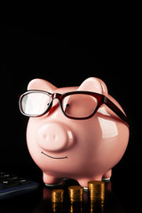 Piggy bank with glasses,coins and calculator on a black background