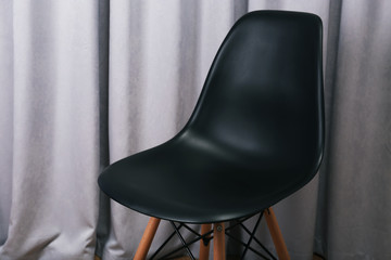 Stylish black chair on grey curtains background