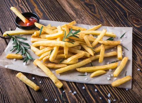 French fries with ketchup and rosemary on wooden background