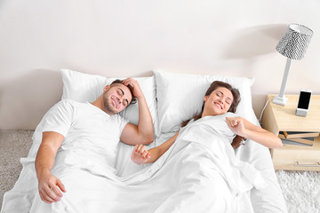Happy couple waking up with mobile alarm clock