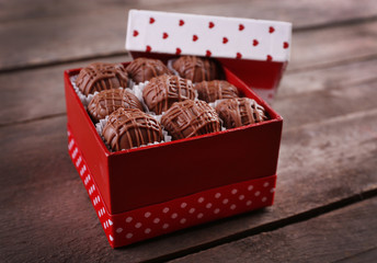 Chocolate candies in beautiful gift box on wooden background, close up