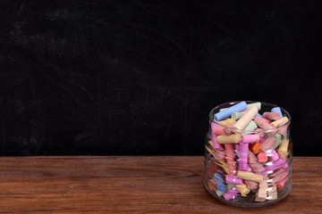 Glass jar of coloured chalk in front of blackboard