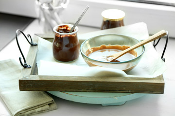 Melted chocolate on glass bowl on tray, on wooden background