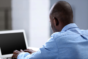 African American businessman in blue shirt working on laptop, close up