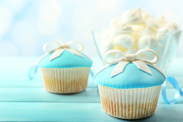 Tasty cupcake with bow on color wooden table, on bright background