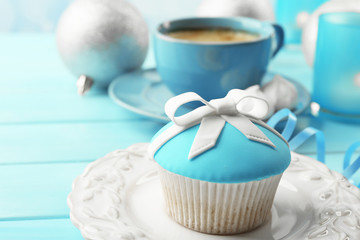 Tasty cupcake with bow, coffee cup and Christmas toys on color wooden background