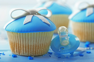 Tasty cupcake with bow and baby pacifier on color wooden background