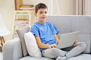 Boy with laptop sitting on a sofa at home