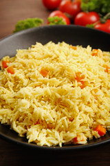 Stewed rice with a carrot on a black plate over wooden background, close up