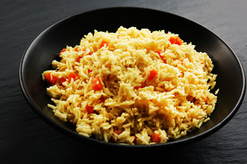 Stewed rice with a carrot on a plate over black background, close up