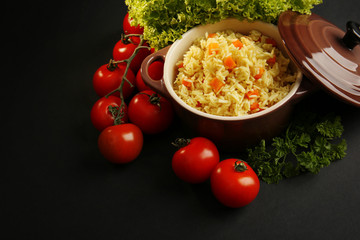 Stewed rice with a carrot and tomatoes in a cooking pot over black background