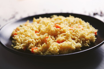 Stewed rice with a carrot on a black plate, close up