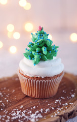 Christmas cupcake on wooden stand with lights on background