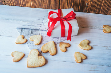 White box with red ribbon, the envelope, cookies in the shape of heart, red candles. Romantic gift on Valentine's Day on wooden background.