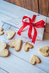 White box with red ribbon, the envelope, cookies in the shape of heart, red candles. Romantic gift on Valentine's Day on wooden background.