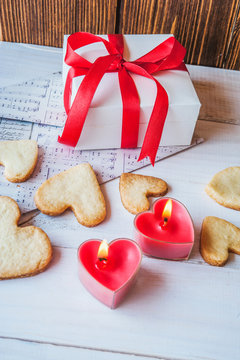 White box with red ribbon, the envelope, meringue, cookies in the shape of heart, red candles. Romantic gift on Valentine's Day on wooden background.