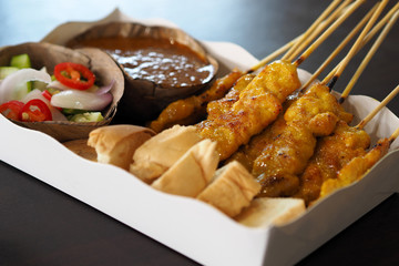 Pork Satay with peanut sauce and cucumber salad on white paper food tray