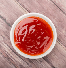 A bowl of thick chili sauce in white bowl over wooden background