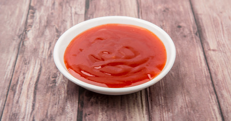A bowl of thick chili sauce in white bowl over wooden background