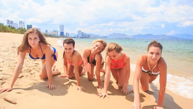 cheerleaders in bikinis crawl in line along sand beach smile