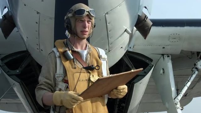 Pilot re-enactor in authentic flight gear checks a flight chart while standing at the front of a US Navy Grumman Avenger from World War II.  Mute.  Recorded in 4K, ultra high definition.