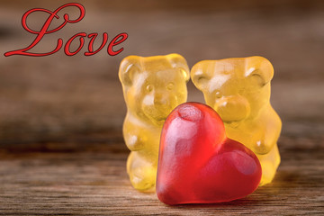 macro two yellow gummy bears with red hearts and writing love on wood