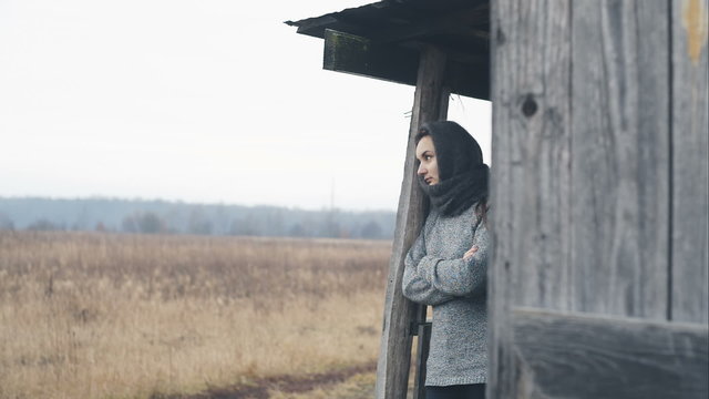 Lonely poor woman is on the threshold of old wooden house. RAW video record.