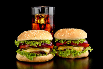 Big two cheeseburgers with glass of cola on black wooden table