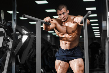 Fototapeta na wymiar Muscular bodybuilder working out in gym relaxing after triceps exercises on parallel bars