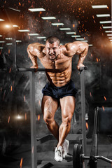 Muscular bodybuilder working out in gym doing triceps exercises on parallel bars