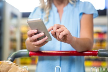 Woman with cart using smartphone 