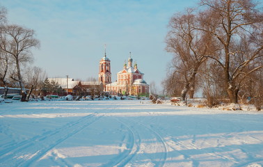 Rural winter landscape with a church, a frozen river and houses on the riverbank