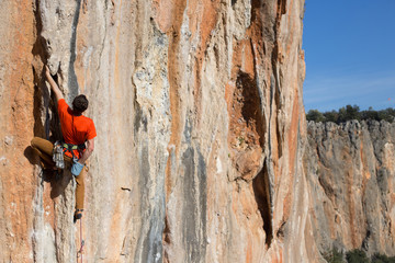 Young man climbing on a limestone wall with wide valley on the background