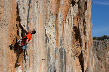 Young man climbing on a limestone wall with wide valley on the background