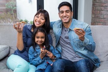 Smiling family eating pizza on the sofa