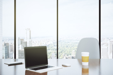 Modern desk in an office with a blank laptop and a large window