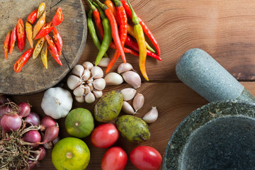 Thailand Food Ingredients: Tomatoes, peppers, garlic, shallots, lemon, olive with a mortar on a wooden floor.