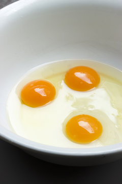 Drei aufgeschlagene rohe Eier in einer weißen Schüssel