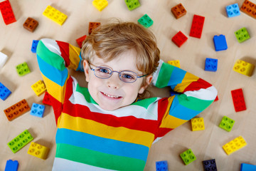 Little blond child playing with lots of colorful plastic blocks