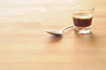 bicchierino di caffe con cucchiaino di zucchero su tavolo di legno, illuminato posteriormente dalla...