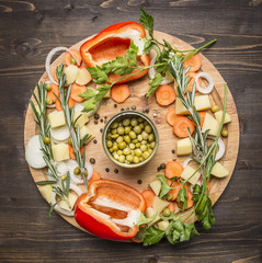 bell peppers, canned peas, sliced carrots, potatoes and herbs on a cutting board on wooden rustic background top view vegetarian concept