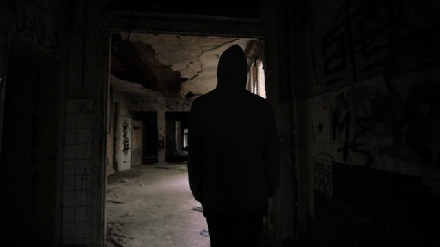 Slow motion of a guy with hood walking through abandoned building