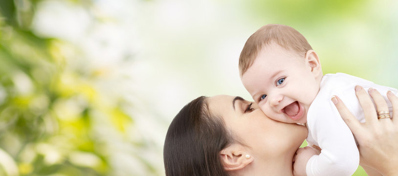 happy mother kissing baby over green background