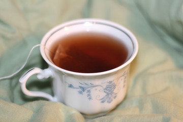 Cup of tea with tea bag on the bed.