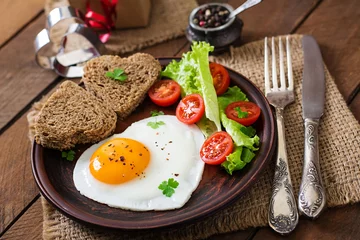 Photo sur Plexiglas Oeufs sur le plat Petit-déjeuner le jour de la Saint-Valentin - œufs au plat et pain en forme de cœur et légumes frais.