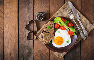 Frühstück am Valentinstag - Spiegeleier und Brot in Herzform und frisches Gemüse. Ansicht von oben