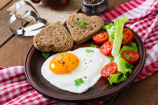 Breakfast on Valentine's Day - fried eggs and bread in the shape of a heart and fresh vegetables.